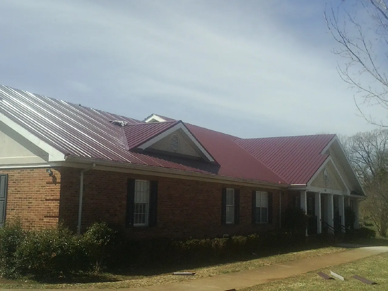 Red metal roof with gabled entries on a long brick building, from a Hail Damage Roof Repair job in Center Ossipee