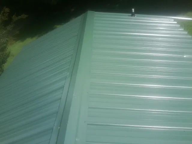New green metal panels meeting at the ridge of a roof — Flat Roof Repair work by our crew in Center Ossipee