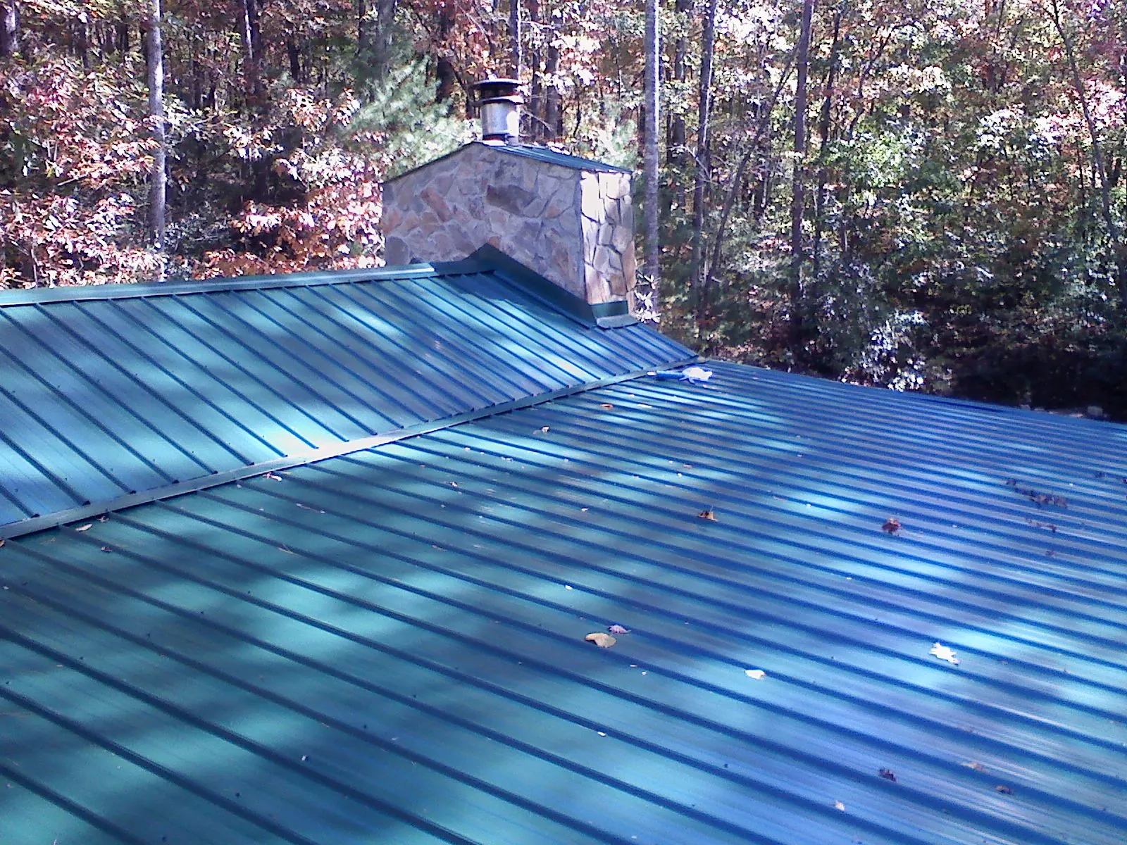 New green metal roof and stone chimney surrounded by autumn woods in Center Ossipee