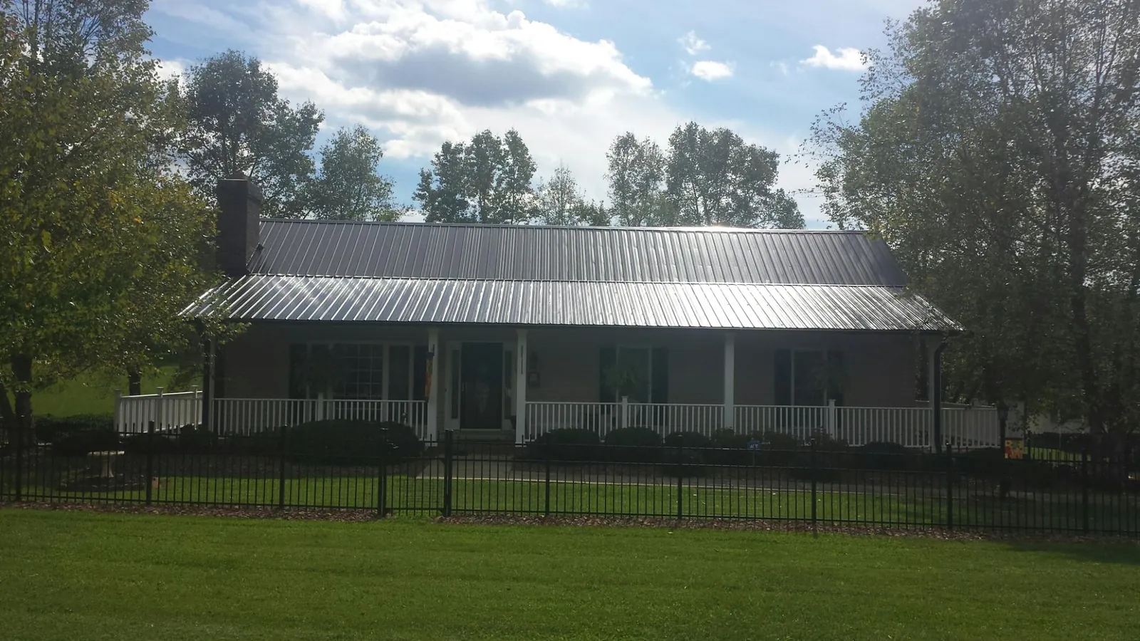 Gray metal roof on a brick ranch with a full width front porch — Gutter Guard Installation work by our crew in Center Ossipee