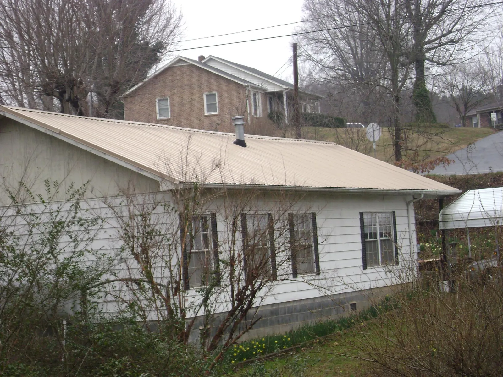 Tan metal roof on a white sided house set into a hillside — Commercial Roofing by Roofing Brothers in Center Ossipee