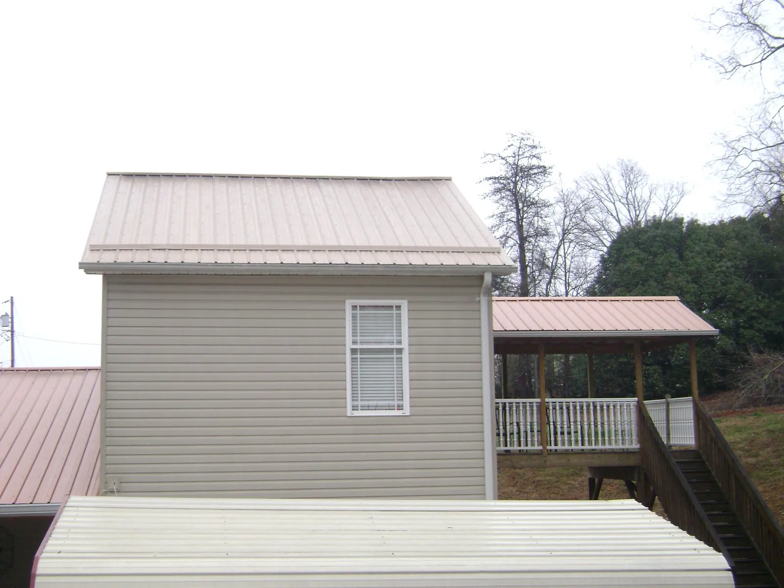 Tan metal roofs on a two story addition and attached porch, from a Roof Replacement job in Center Ossipee